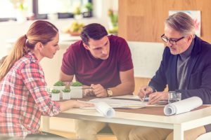 Architect with clients discussing blueprint, blueprint rolled on table.